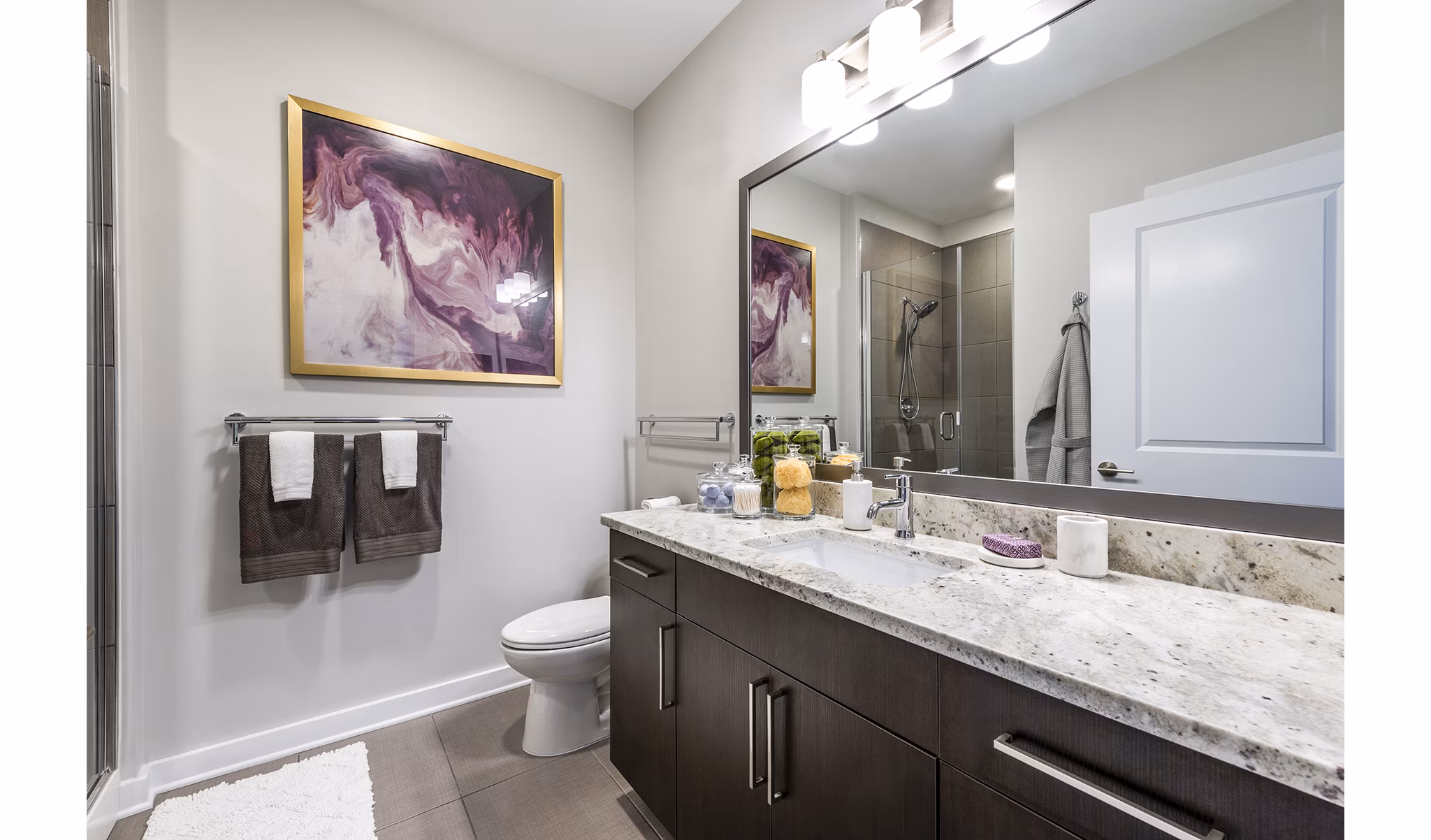 Modern bathroom featuring a large mirror and granite countertop in luxury apartments
