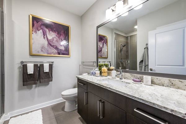 Modern bathroom featuring a large mirror and granite countertop in luxury apartments