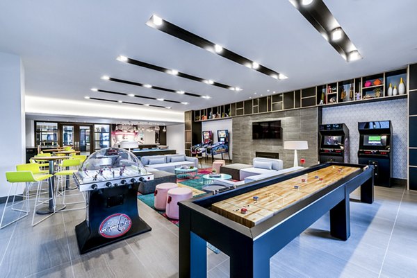 Modern game room with arcade machines, shuffleboard table, and seating areas at luxury apartments