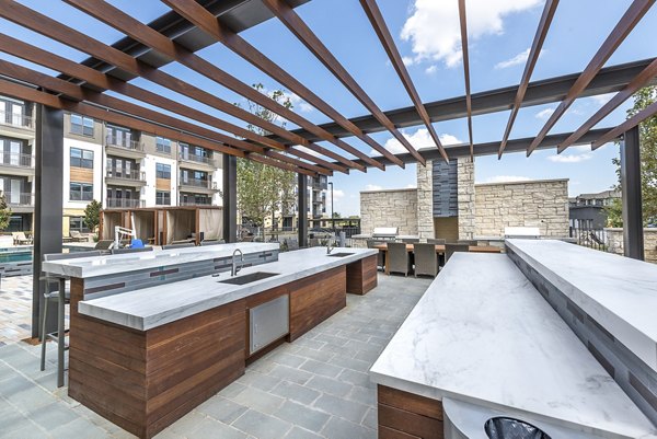 Outdoor grill area at Overture Fairview Apartments with modern seating and lush landscaping, ideal for social gatherings and relaxation