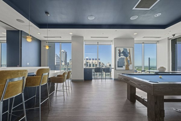 Clubhouse game room with pool table and lounge area at Skyhouse Uptown North Apartments