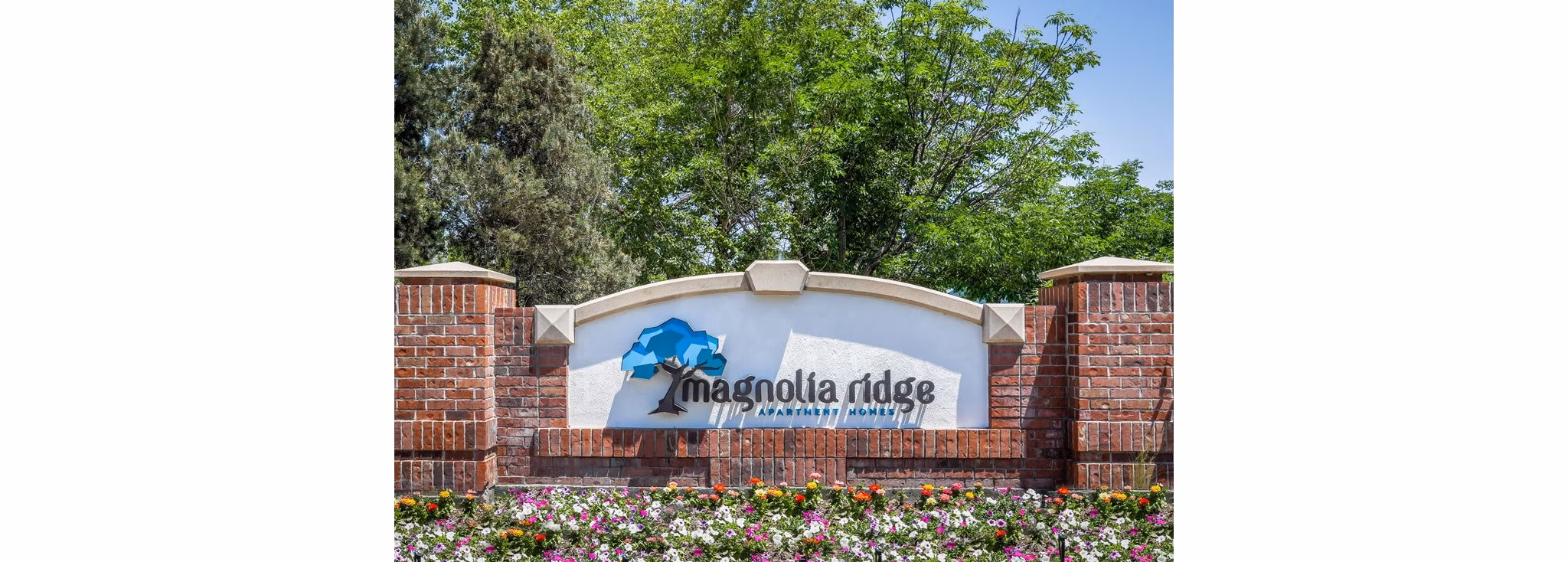 Magnolia Ridge Apartment Homes sign surrounded by vibrant flowers and lush trees