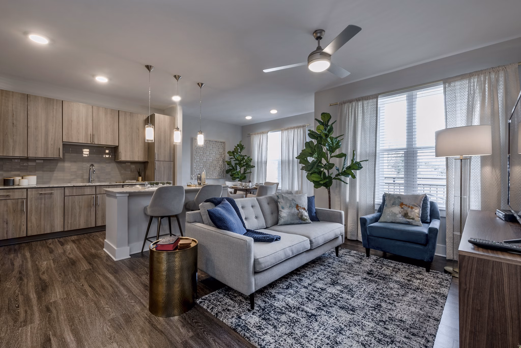 Modern living room and kitchen with wooden flooring, gray sofa, and dining table in luxury apartments