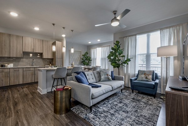 Modern living room and kitchen with wooden flooring, gray sofa, and dining table in luxury apartments