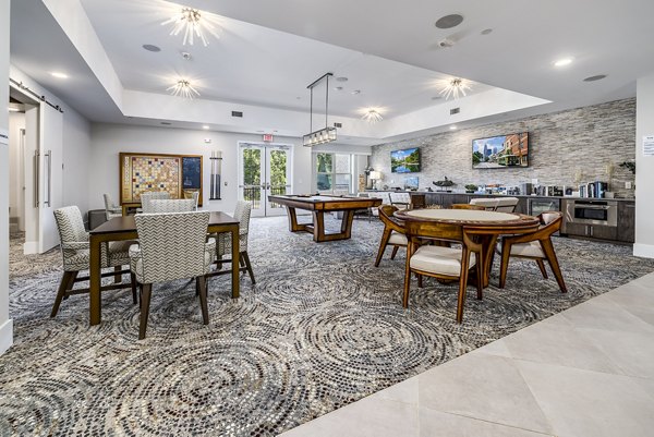 Modern communal room with tables, chairs, a pool table, and kitchenette in luxury apartments