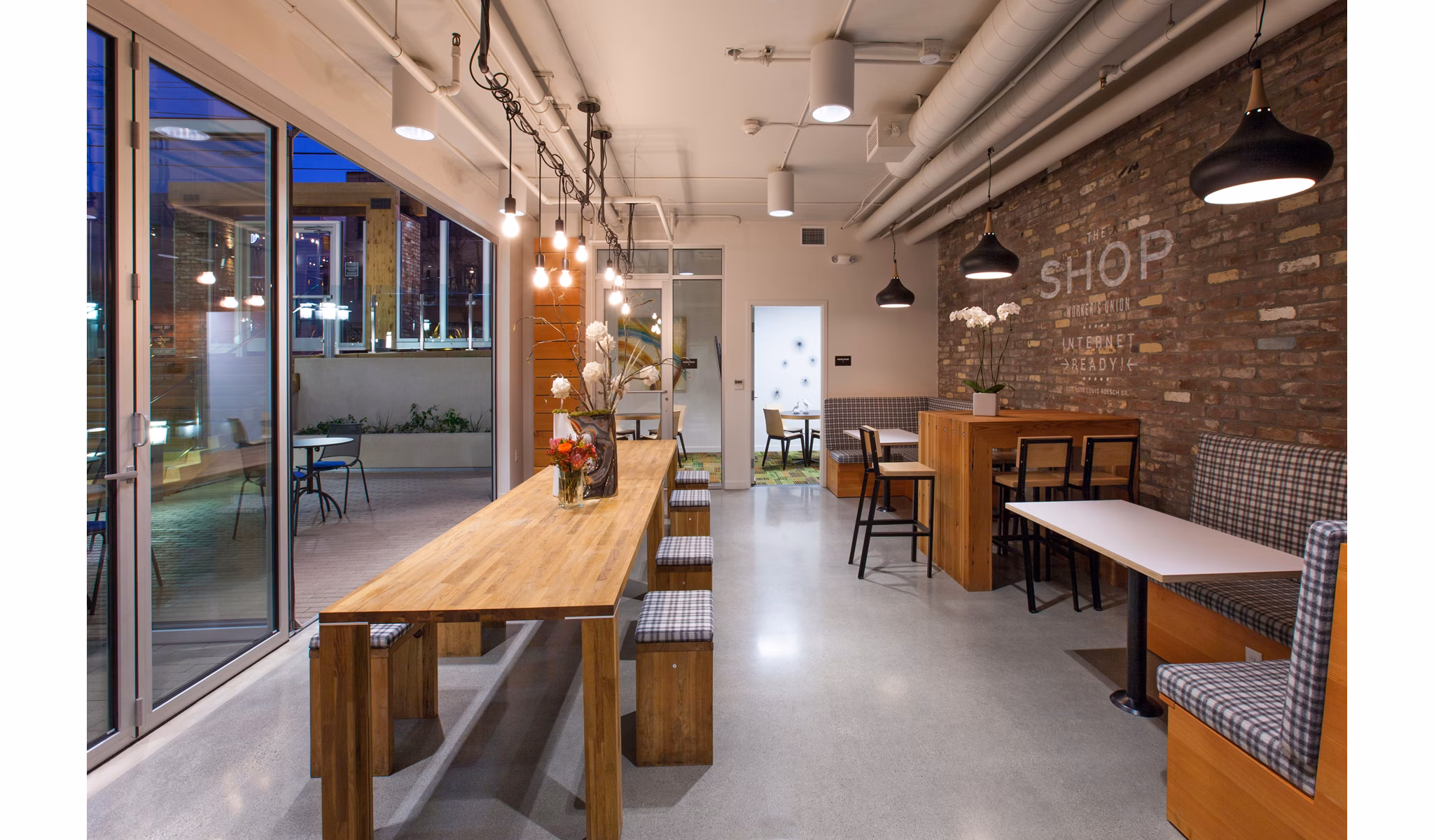 Modern dining area with wooden tables and pendant lighting in luxury apartments, featuring decorative flowers and a stylish brick wall