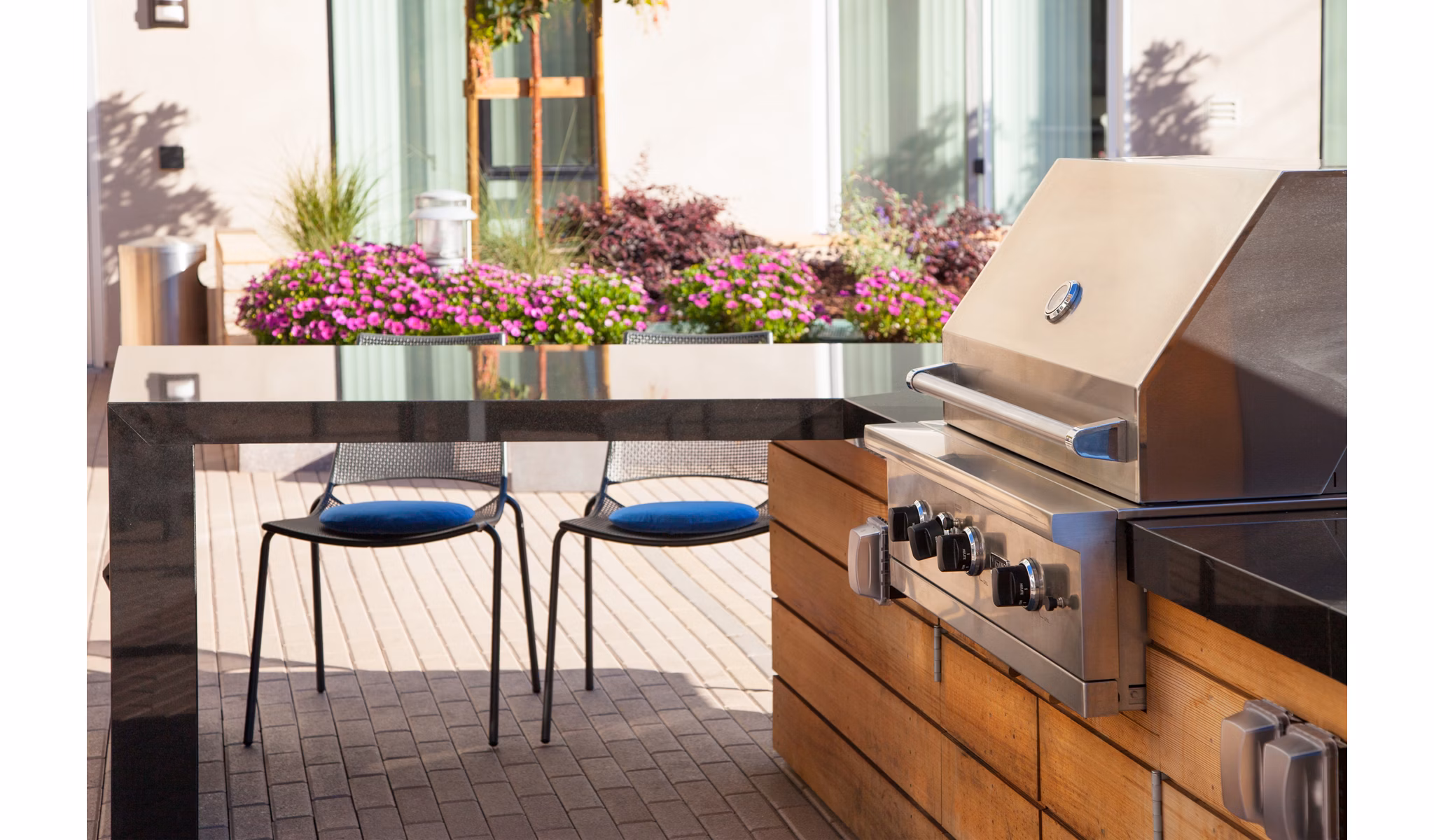 Outdoor patio area featuring a grill and seating surrounded by flowers at luxury apartments