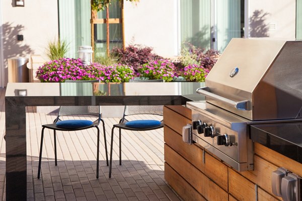 Outdoor patio area featuring a grill and seating surrounded by flowers at luxury apartments