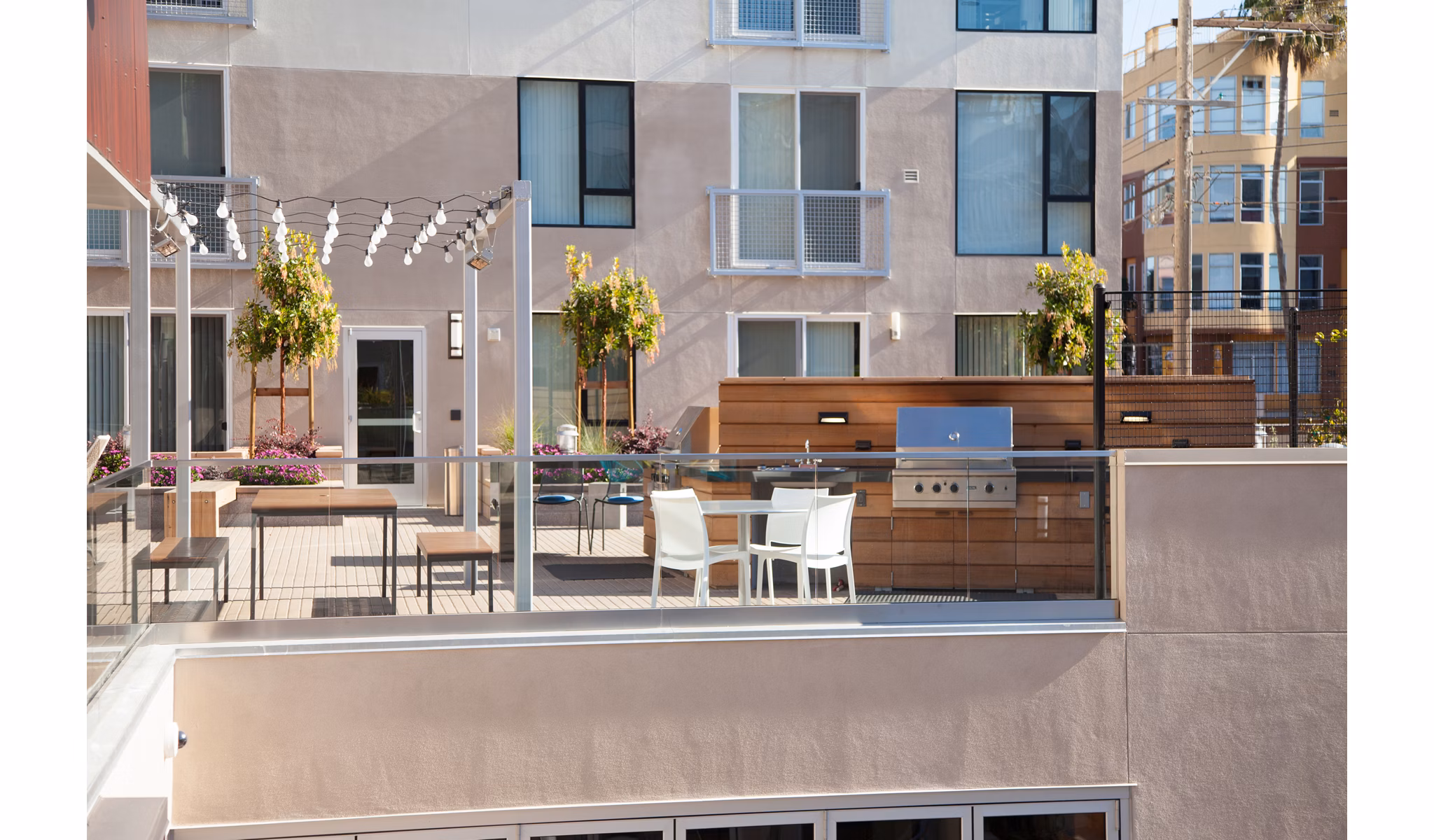 Outdoor patio with dining table, chairs, and grill, surrounded by plants and string lights at luxury apartments