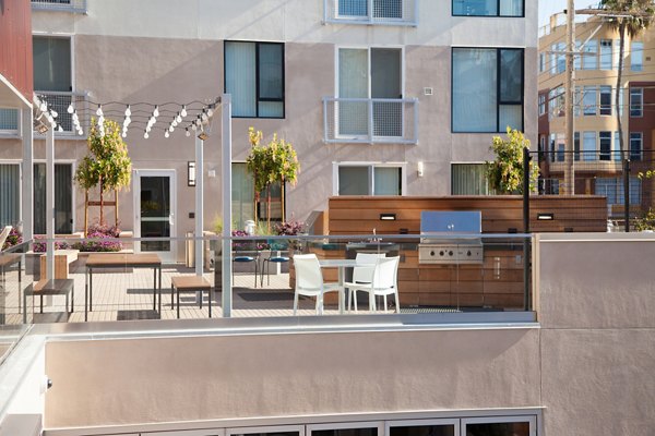 Outdoor patio with dining table, chairs, and grill, surrounded by plants and string lights at luxury apartments