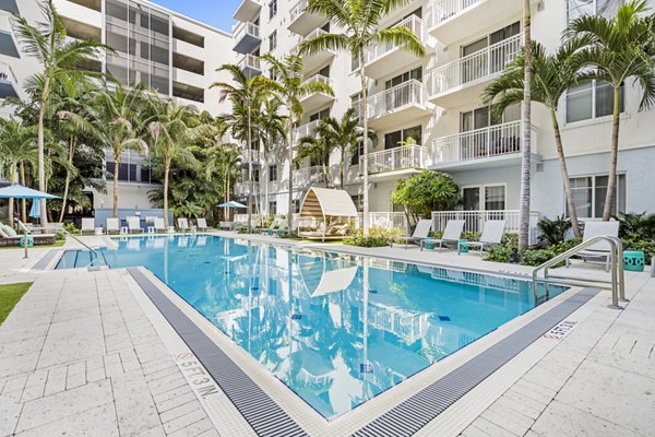 Sunlit outdoor pool at Boca City Walk Apartments with lounge chairs and vibrant landscaping