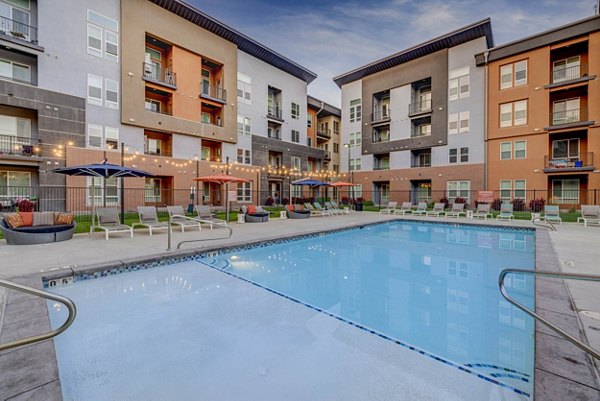 Resort-style pool at Novi at Jordan Valley Station Apartments with lounge chairs and lush landscaping