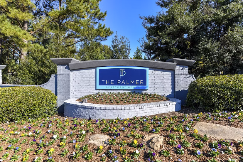 The Palmer Apartment Homes: Welcoming sign surrounded by lush landscaping in a serene community
