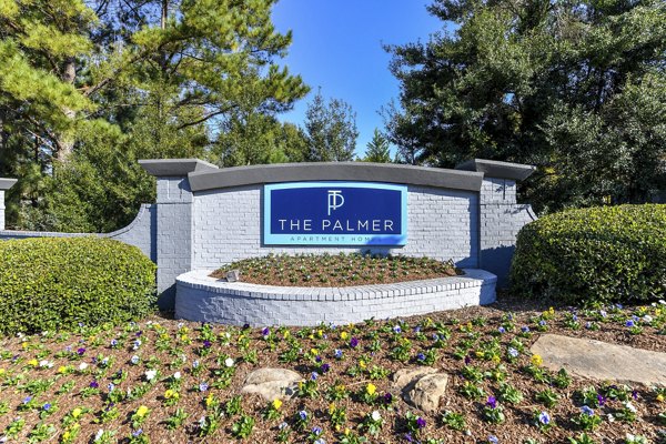 The Palmer Apartment Homes: Welcoming sign surrounded by lush landscaping in a serene community