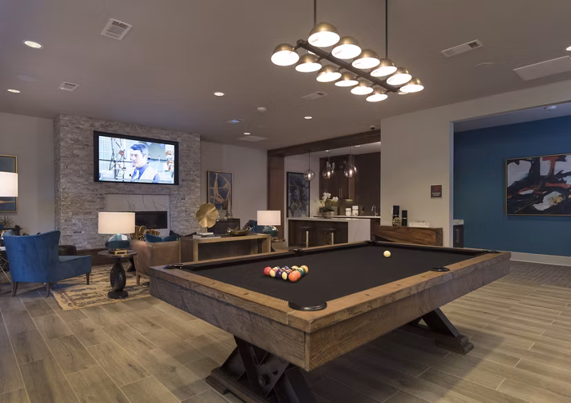 Spacious living room featuring a pool table and stone wall TV at luxury apartments