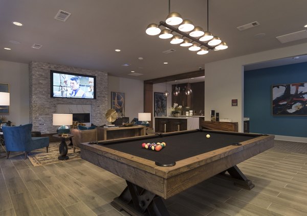 Spacious living room featuring a pool table and stone wall TV at luxury apartments