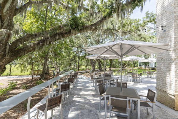 Outdoor patio with modern seating at Overture West Ashley Apartments, featuring lush greenery and ambient lighting