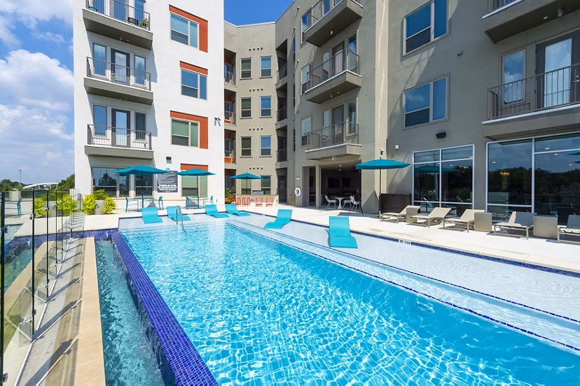 Imagery of a gleaming pool bathed in sunlight, surrounded by lush greenery at the luxury Encore Montrose Apartments
