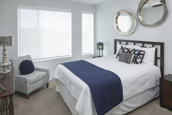 Cozy bedroom featuring plush bedding and large windows at Alexan LoHi Apartments â€“ luxury living in the heart of Denver