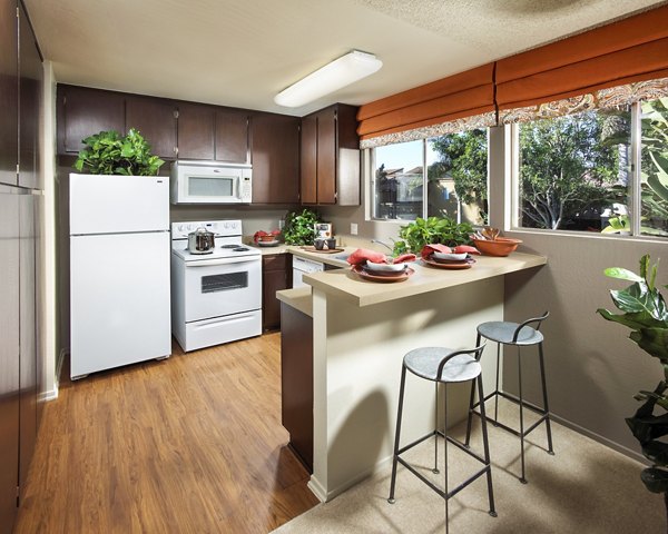 Modern kitchen with dark wood cabinets and a small bar with stools, featuring white appliances and decorative plants