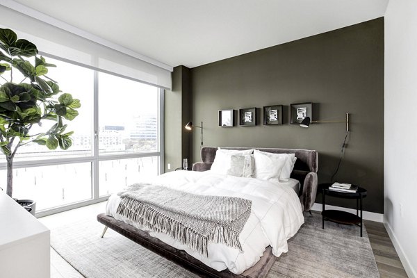 Harbor 1500 Apartments: Bright bedroom featuring large window, green accent wall, and plants in luxury Greystar apartments