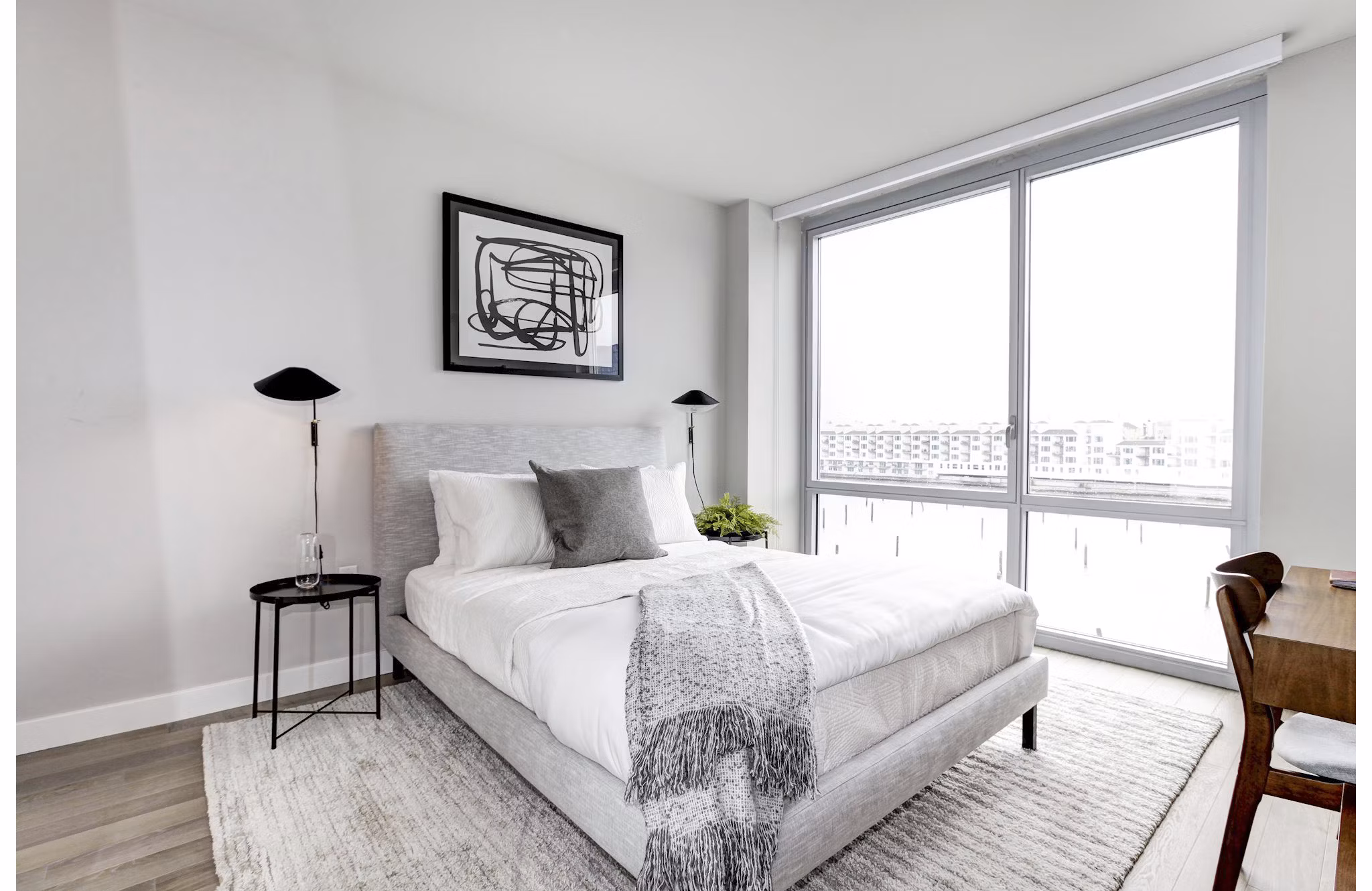 Bright bedroom with large windows, abstract art, and minimalist decor at Harbor 1500 Apartments