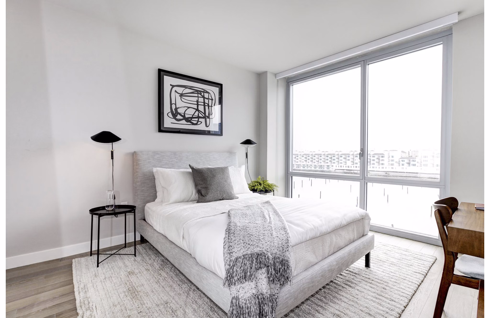 Bright bedroom with large windows, abstract art, and minimalist decor at Harbor 1500 Apartments
