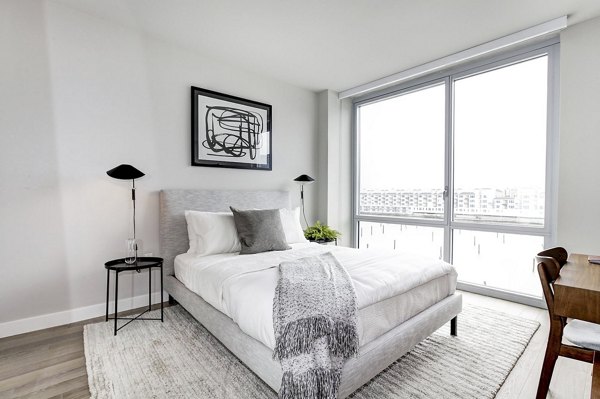 Bright bedroom with large windows, abstract art, and minimalist decor at Harbor 1500 Apartments