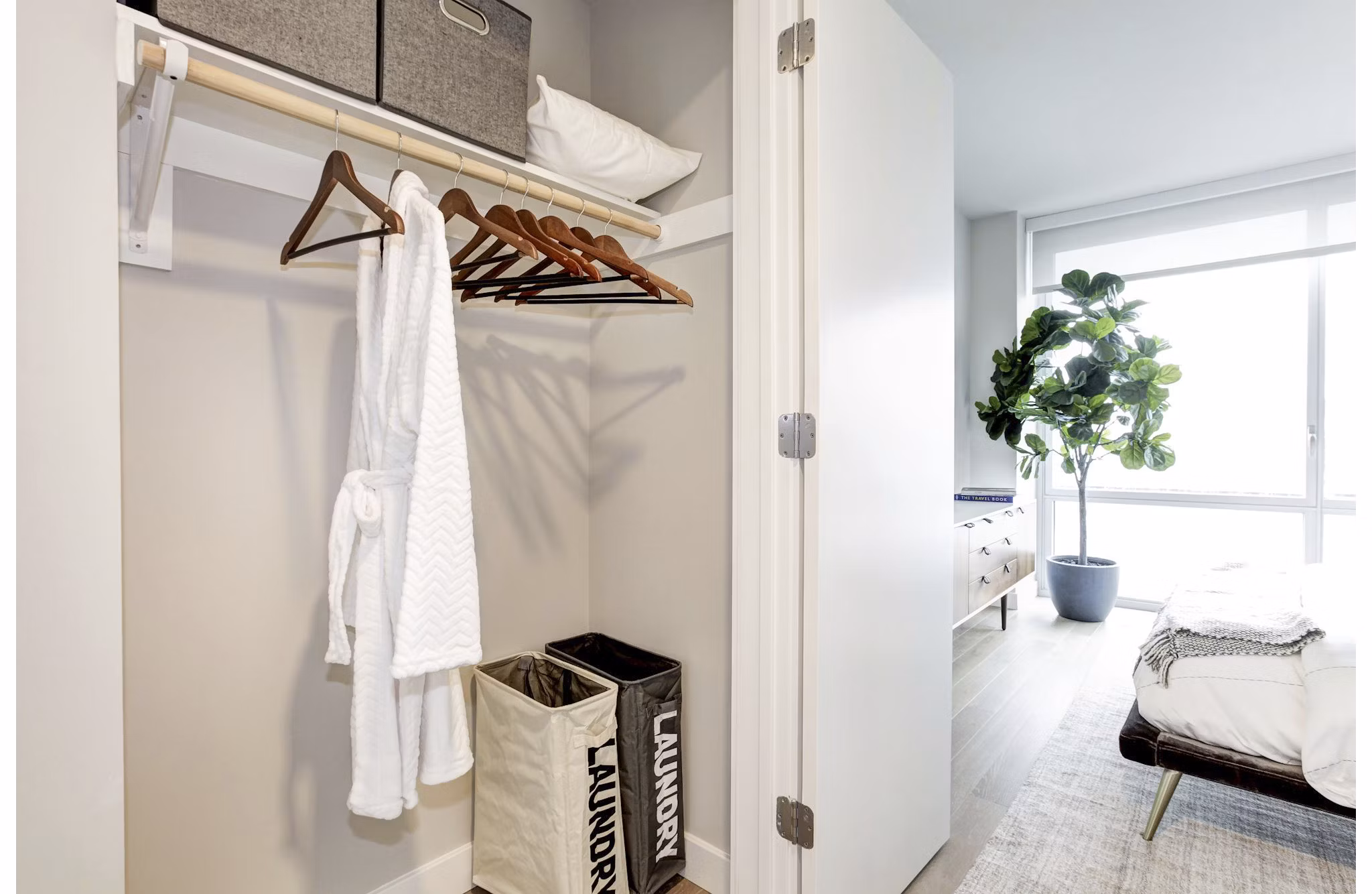Open closet with robe, hangers, and laundry bins, offering a bedroom view at Harbor 1500 Apartments
