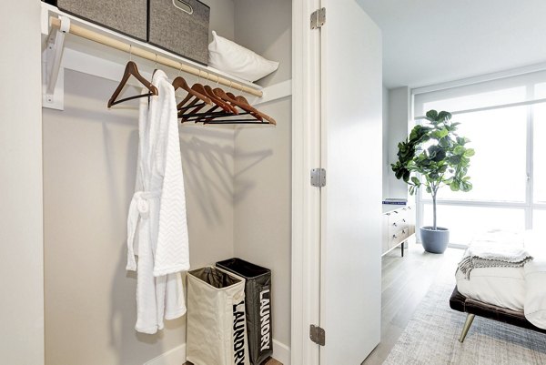 Open closet with robe, hangers, and laundry bins, offering a bedroom view at Harbor 1500 Apartments