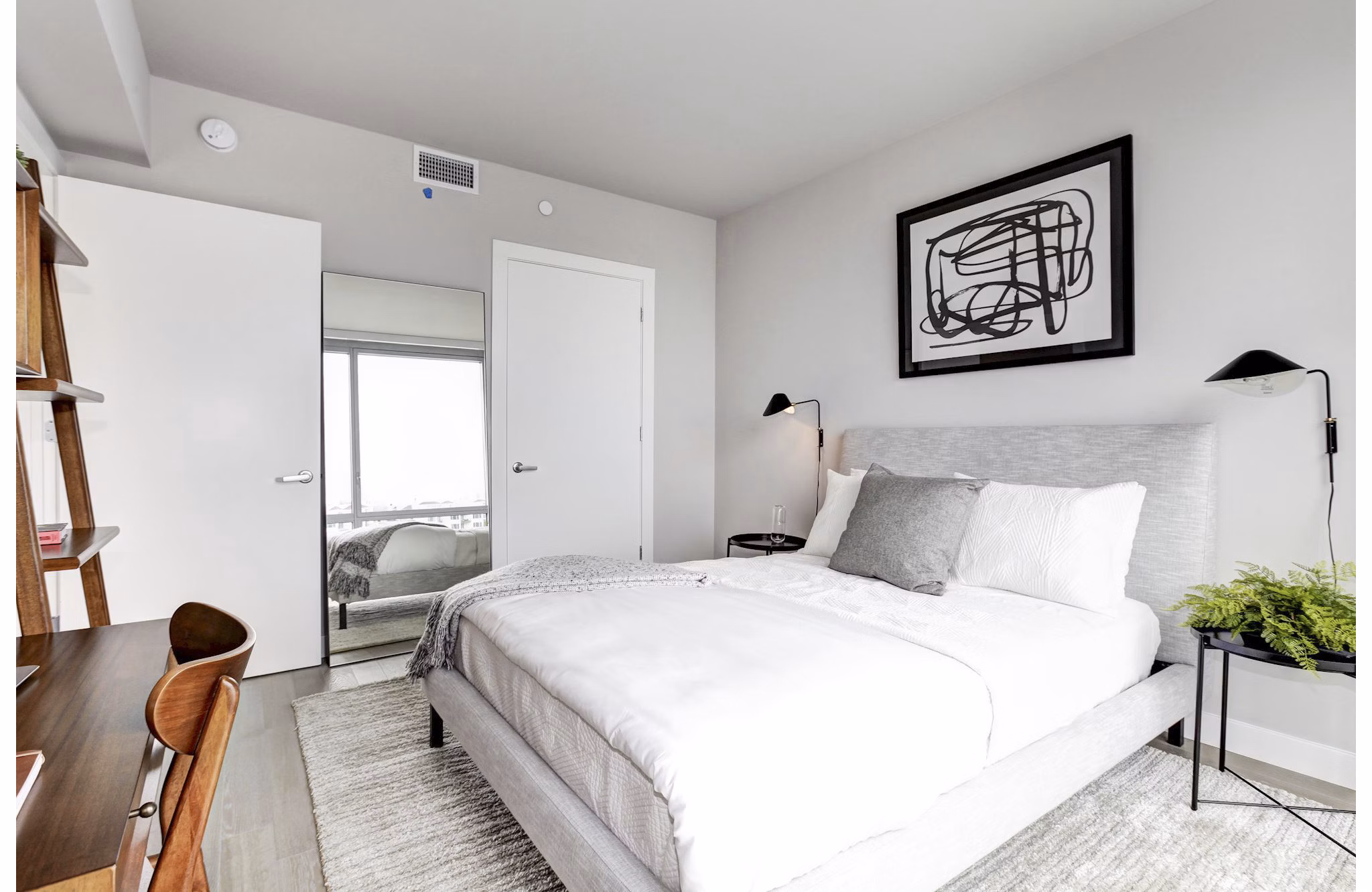 Minimalist bedroom with white bed, abstract art, and desk at Harbor 1500 Apartments in Weehawken, offering serene luxury living spaces