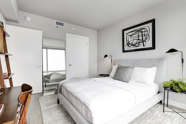 Minimalist bedroom with white bed, abstract art, and desk at Harbor 1500 Apartments in Weehawken, offering serene luxury living spaces