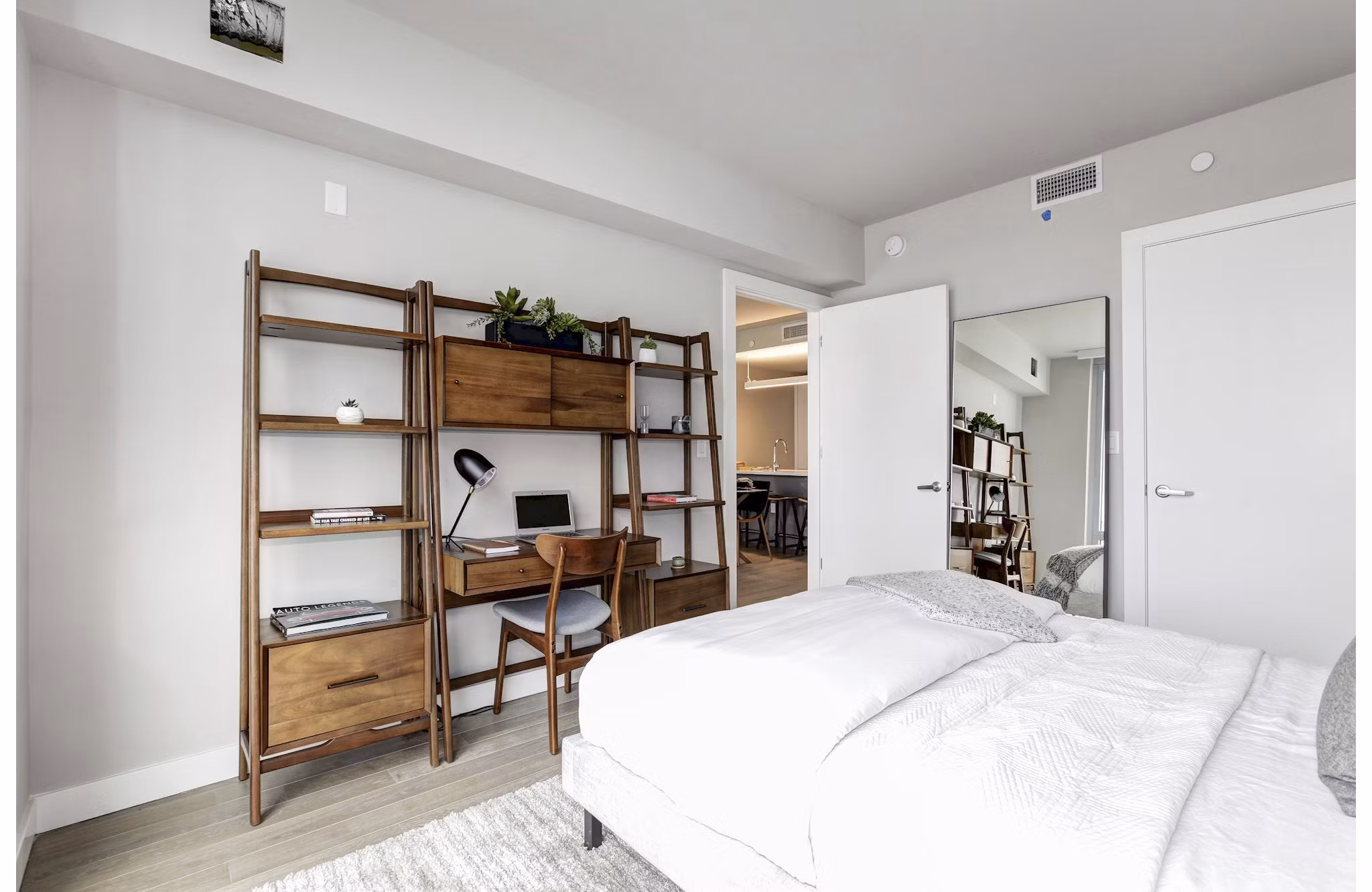 Cozy bedroom featuring wooden desk, shelves, and white bedding at Harbor 1500 Apartments