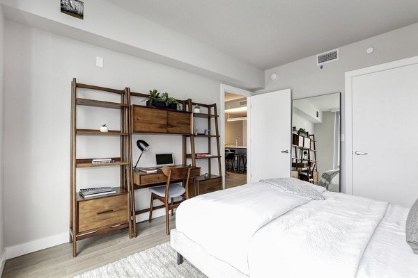 Cozy bedroom featuring wooden desk, shelves, and white bedding at Harbor 1500 Apartments