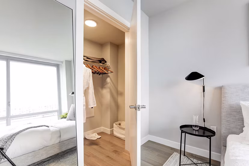 Bedroom featuring open closet, bed, and side table at Harbor 1500 Apartments Luxurious interior design in Greystar luxury apartments