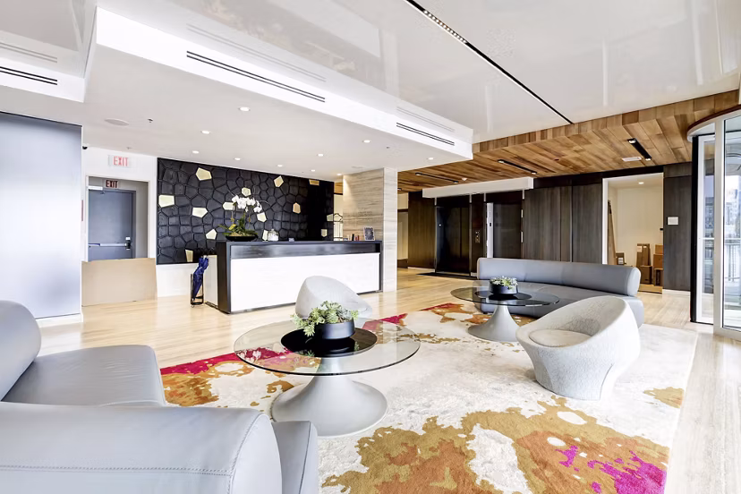 Bright lobby featuring sleek furniture, geometric wall, and vibrant rug at Harbor 1500 Apartments