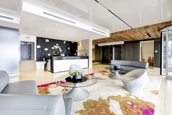 Bright lobby featuring sleek furniture, geometric wall, and vibrant rug at Harbor 1500 Apartments