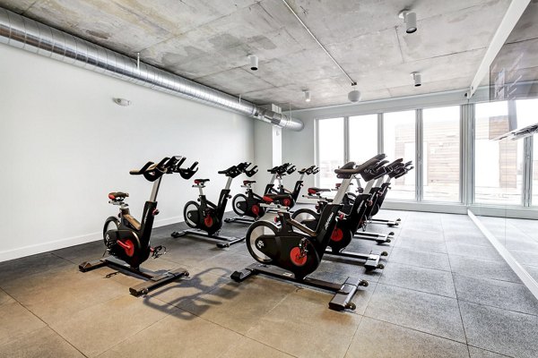 Indoor cycling studio with multiple stationary bikes and large windows at Harbor 1500 Apartments