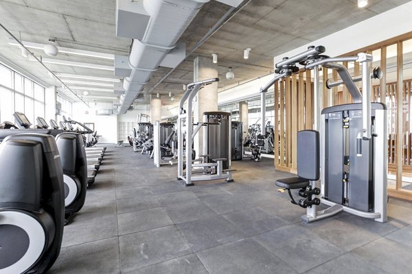 Spacious gym with various exercise machines and large windows at Harbor 1500 Apartments in Weehawken, perfect for fitness enthusiasts