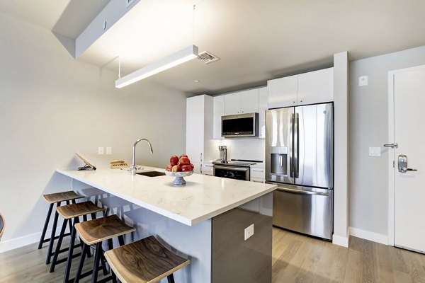 Sleek kitchen with island, bar stools, and stainless steel appliances at Harbor 1500 Apartments in luxury complex