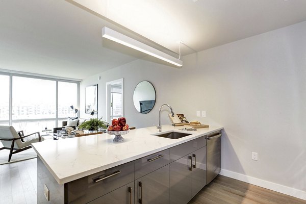 Harbor 1500 Apartments: Sleek kitchen featuring an island, white countertops, and large windows in luxury apartment