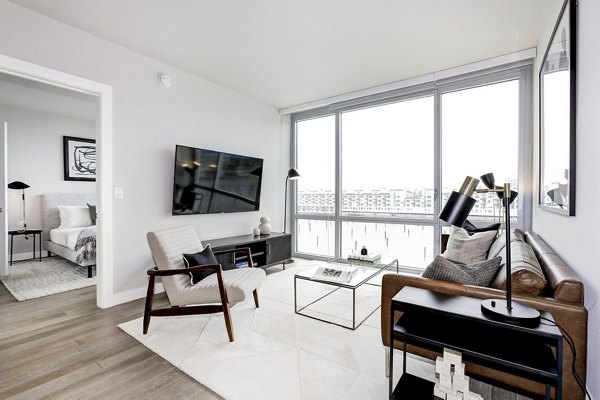 Spacious, bright living room with large windows, stylish furniture, and TV in Harbor 1500 Apartments â€“ luxury apartments by Greystar