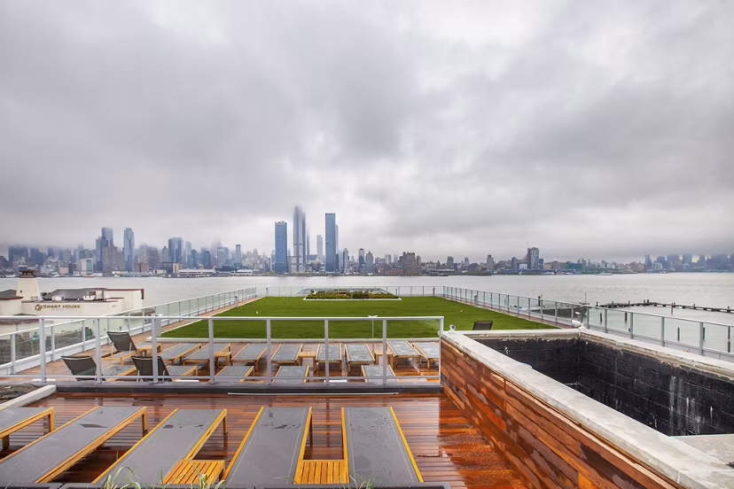 Rooftop terrace with seating and city skyline view at Harbor 1500 luxury apartments, featuring a green lawn