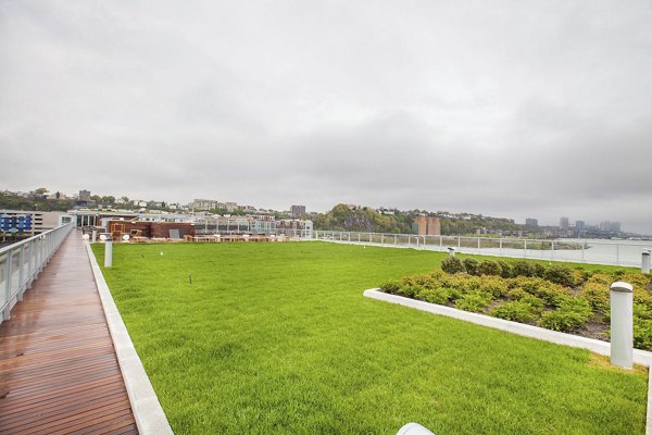 Rooftop garden with green lawn and wooden walkway on cloudy day at Harbor 1500 Apartments