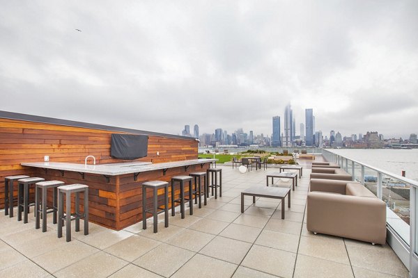 Rooftop patio with seating, bar, and city skyline view at Harbor 1500 Apartments in Weehawken, offering luxurious amenities for residents