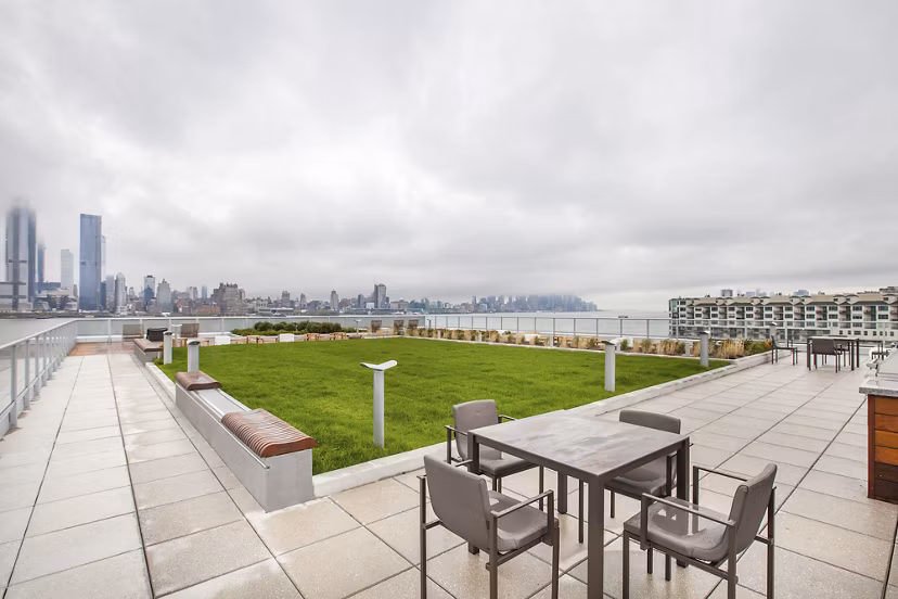 Rooftop terrace with seating, green lawn, and city skyline view at Harbor 1500 luxury apartments