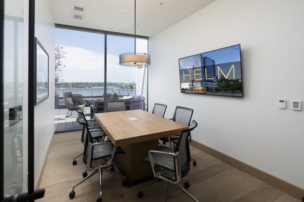 Meeting room featuring modern seating and large presentation screen at Helm Apartments