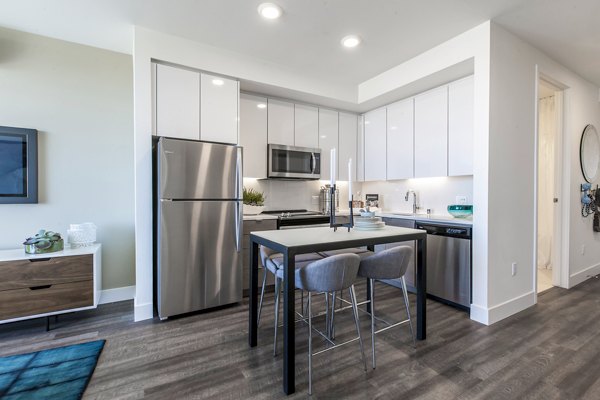 Modern kitchen with dark cabinets, stainless steel appliances, a small dining table with two chairs, and place settings