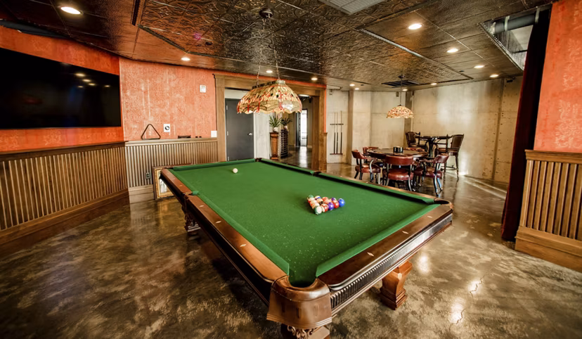 Game room with pool table and arcade games at Hardware Village Apartments, featuring modern decor and comfortable seating