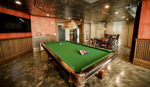 Game room with pool table and arcade games at Hardware Village Apartments, featuring modern decor and comfortable seating
